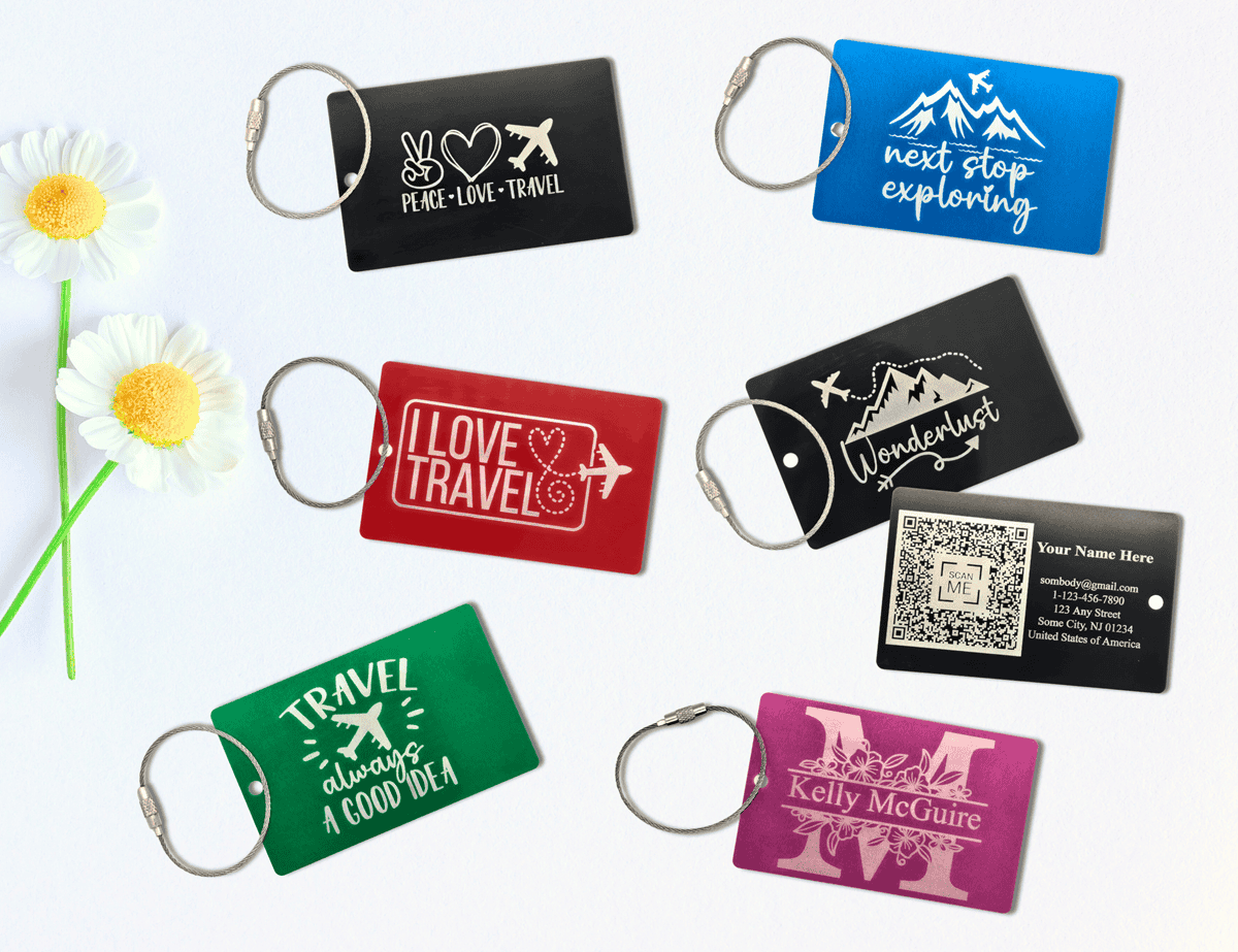 Assorted engraved luggage tags with key rings, featuring travel quotes, personalized names, and QR code contact info.