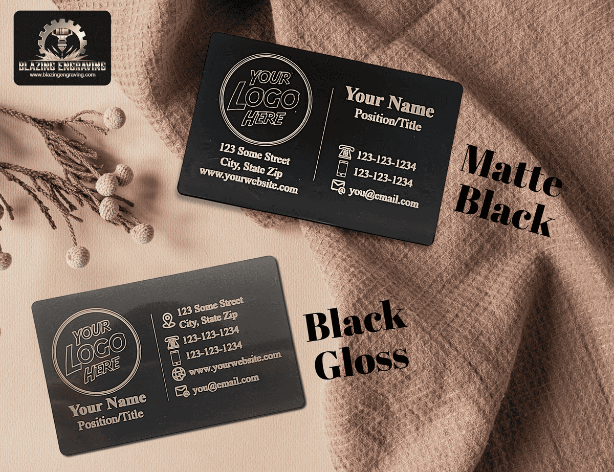 Two custom laser-engraved metal business cards from Blazing Engraving, shown in matte black and black gloss finishes, displayed on textured beige and brown fabrics.
