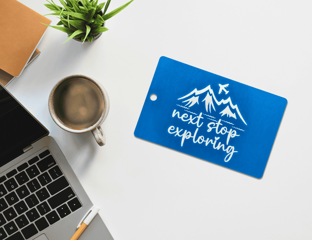 Blue engraved luggage tag with mountain and airplane design, reading “next stop exploring.”