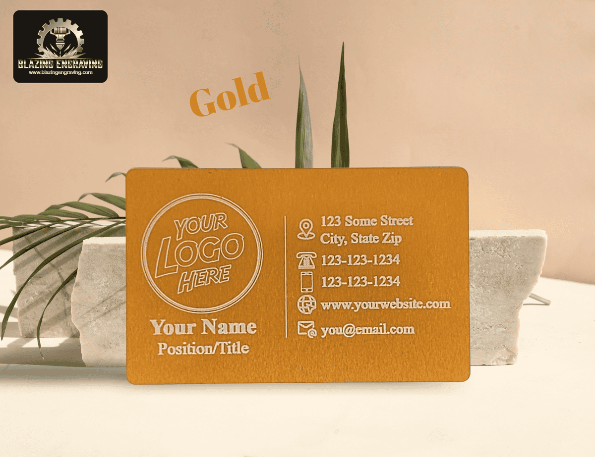 Custom laser-engraved metal business card in gold finish with space for logo, name, and contact details, displayed on a stone stand with green leaves.