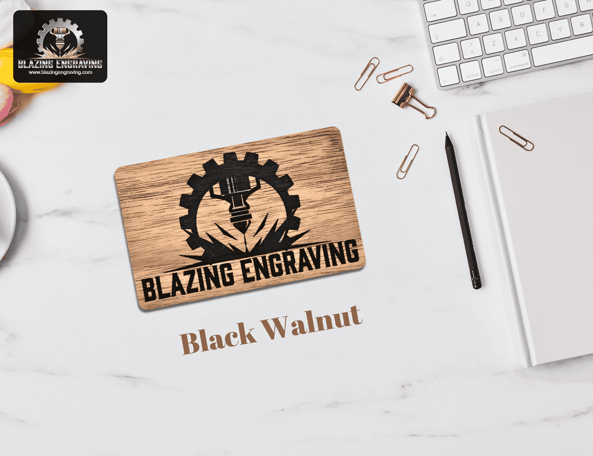 Blazing Engraving business card made of black walnut wood, engraved with the company’s gear and laser logo, displayed on a marble desk with office supplies.