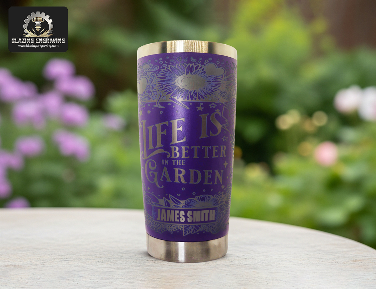 Purple engraved tumbler with floral designs and “Life is Better in the Garden” text, on a table with blurred garden flowers in the background.