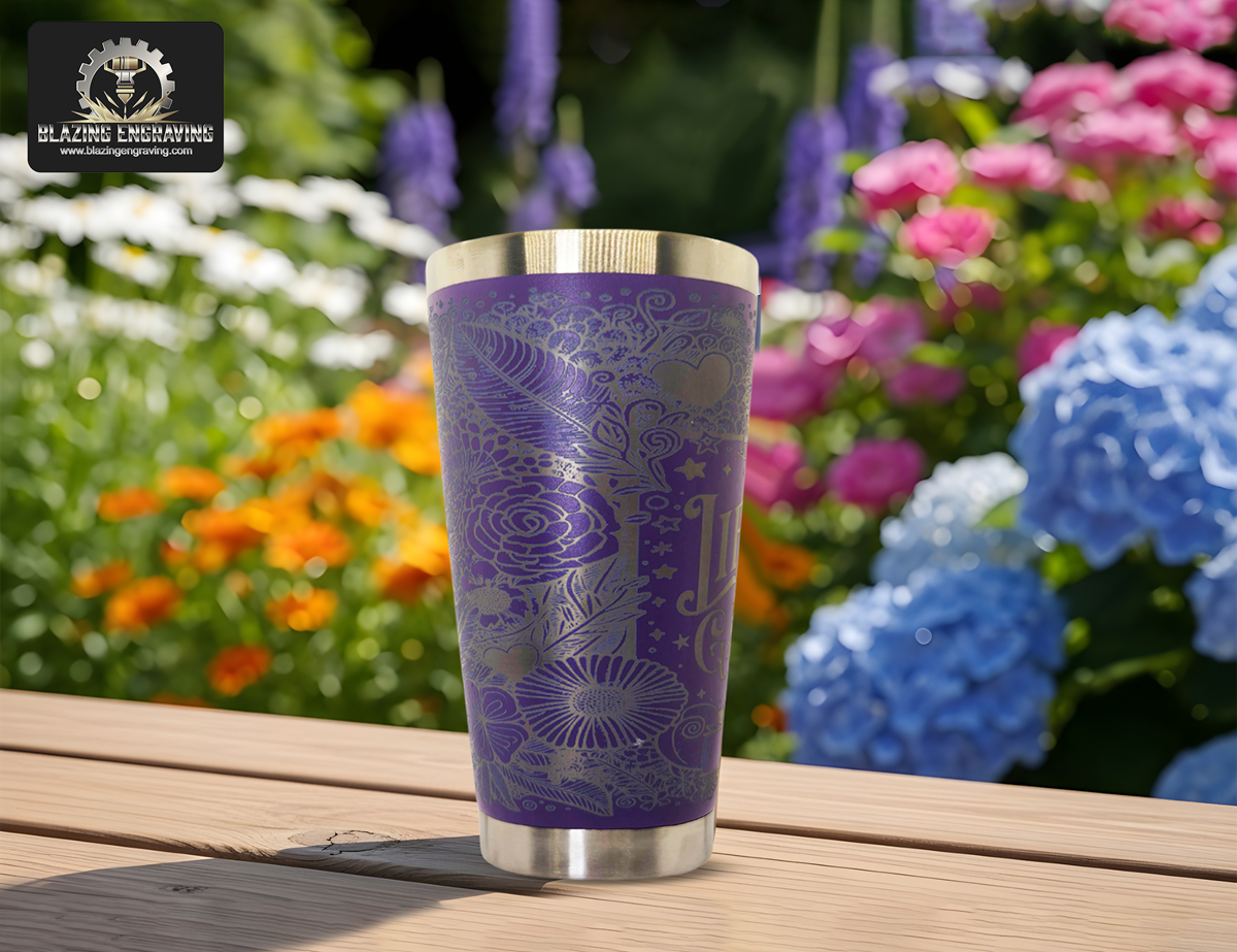 Purple engraved tumbler with floral patterns on a wooden table, surrounded by blooming garden flowers.