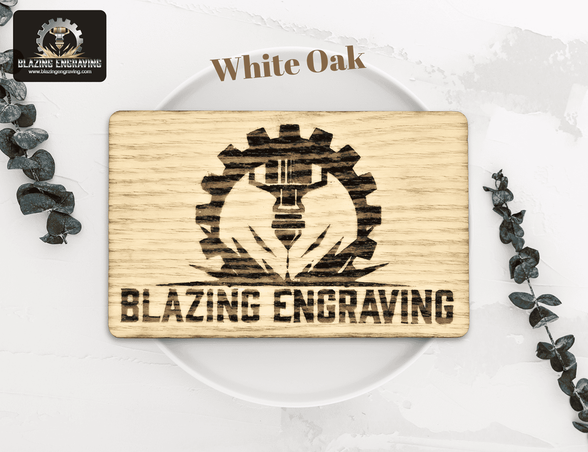 White oak business card from Blazing Engraving, engraved with the company’s gear and laser logo, presented on a white plate with green foliage accents.