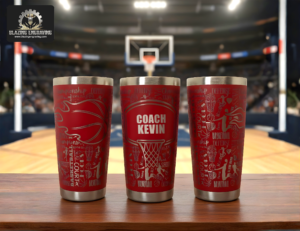 Three stainless steel tumblers showing all sides of a laser-engraved basketball design, personalized with the title "Coach" and the name "Kevin," displayed on a surface with a basketball court in the background. Blazing Engraving logo in the top left corner.