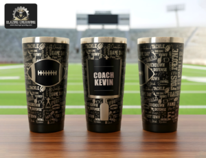 Three stainless steel tumblers showing all sides of a laser-engraved football design, personalized with the title "Coach" and the name "Kevin," displayed on a surface with a football stadium in the background. Blazing Engraving logo in the top left corner.